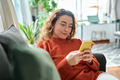 Smiling relaxed young woman sitting on couch using mobile phone technology. - PhotoDune Item for Sale