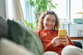 Smiling pretty young woman sitting on couch using mobile cell phone technology. - PhotoDune Item for Sale