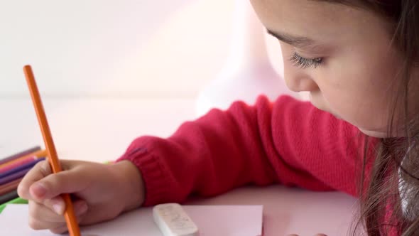 A girl puts down an orange pencil, picks up a blue marker and continues drawing.