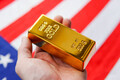 The gold bar in man's hand on the national flag of USA background. Gold Reserve concept. - PhotoDune Item for Sale