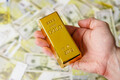 Man holds gold bar on a money banknotes background. - PhotoDune Item for Sale