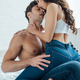 sexy woman in blue jeans and bra looking at camera while sitting on laps of  shirtless boyfriend Stock Photo by LightFieldStudios