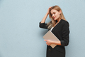 Blonde young business woman wearing black suit over blue plain background, carrying laptop - PhotoDune Item for Sale