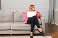 Young Blonde Woman in pink blazer Using a Laptop Computer sitting on Couch at Home - PhotoDune Item for Sale