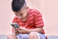 Filipino boy checking mobile phone sitting on the street - PhotoDune Item for Sale