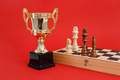 Winner golden cup and Chess board with wooden figures still life on red background - PhotoDune Item for Sale