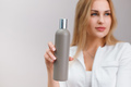 Blonde nurse in white coat hold blank plastic bottle with cosmetics on plain background - PhotoDune Item for Sale
