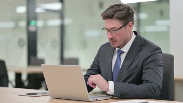 Middle Aged Businessman Standing Up and Going Away From Laptop in Office