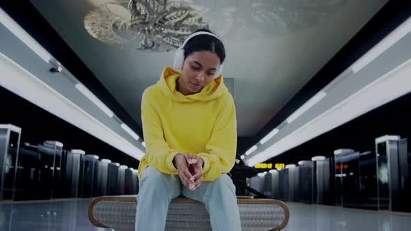 Girl Sitting Waiting for a Train Listening Music in Headphones Clapping Hands