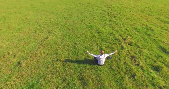 Low Orbital Flight Around Man on Green Grass with Notebook Pad at Yellow Rural Field