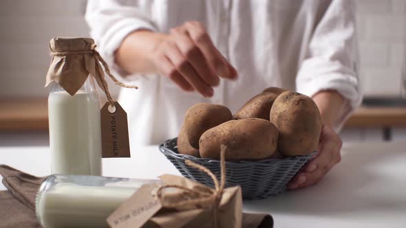 A Woman's Hand Takes A Potato From A Bowl For Cooking, In The Background A Bottle