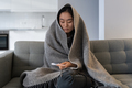 Sad Asian girl trying to warm feel cold ill sick suffering from fever virus sitting on couch at home - PhotoDune Item for Sale