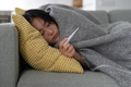 Sick Asian girl lying on sofa wrapped in blanket hold thermometer after infection, covid-19 outbreak - PhotoDune Item for Sale