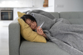 Young sick unhealthy Asian woman suffering from fever measuring temperature while lying on sofa - PhotoDune Item for Sale