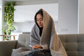 Unhealthy Asian girl sits wrapped in blanket sadly looks at thermometer feels unwell sick after work - PhotoDune Item for Sale
