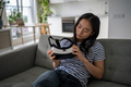 Focused Asian girl sits on home sofa looks at virtual reality glasses for smartphone given by friend - PhotoDune Item for Sale