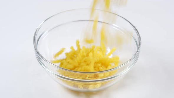 Uncooked fusilli pasta falling into a glass bowl on white background.