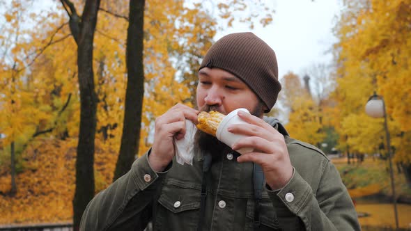 Young Bearded Man Eats Corn with Appetite and Pleasure in the City Park