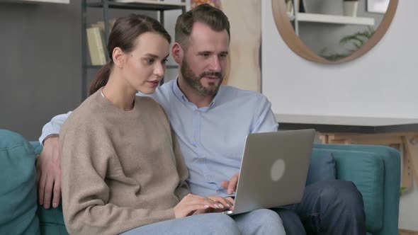 Couple Celebrating Success on Laptop While Sitting on Sofa