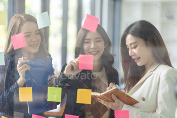 Young creative business Asian woman standing with her colleagues writing new ideas on sticky notes