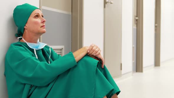 Tensed female surgeon sitting in corridor