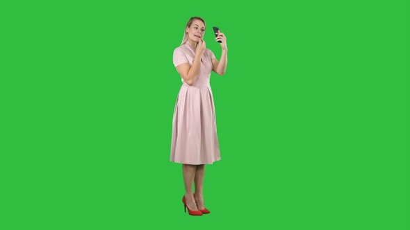 Woman applying lipstick looking at her phone on a Green