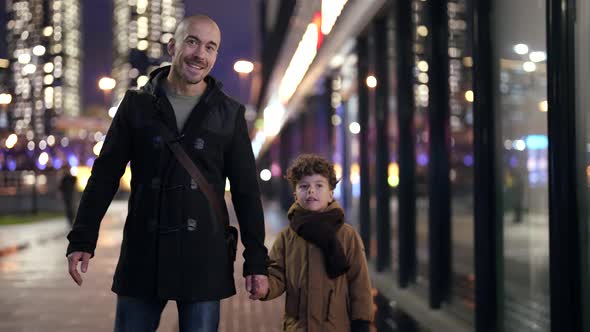 Happy Father and His Preschooler Child are Walking in City in Evening Together