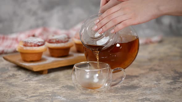 Pour Hot Tea in Glass Cup. A Cup of Tea with Roses Buns, Sweet Buns with Sugar Powder.