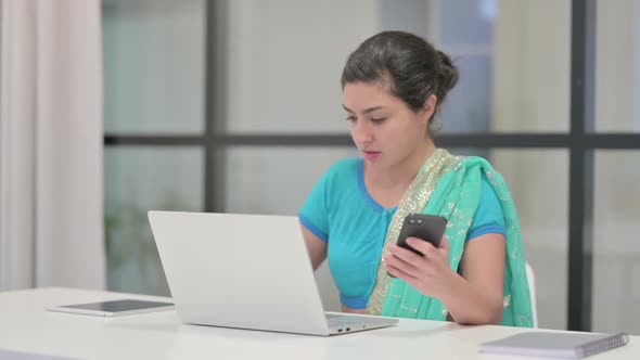 Indian Woman Using Smartphone While Using Laptop in Office