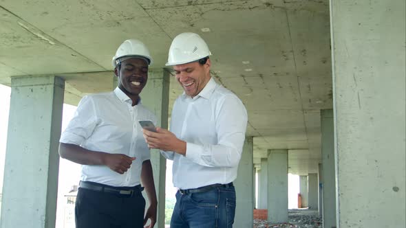 Construction Builders Smiling While Using Smartphone at Site
