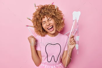 s fist and exclaims loudly celebrates something poses with toothbrushes stuck in curly hair isolated over pink background. Yes finally I achieved it