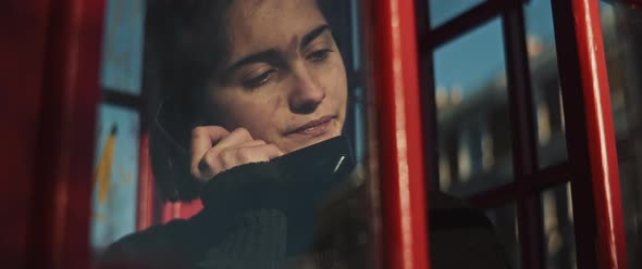 Young woman talking by phone in a phone booth with a serious face