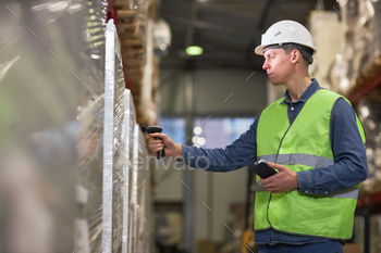 Young male worker doing stock review in warehouse scanning bar codes on boxes