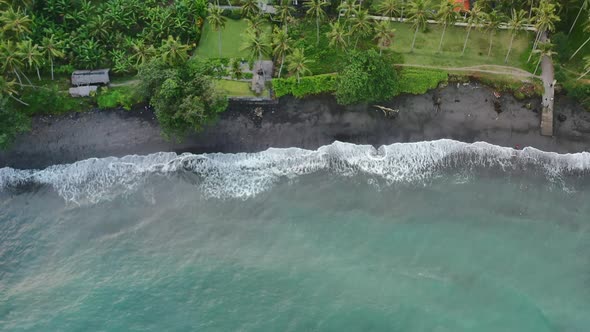 Top down of tropical Jasri beach with turquoise ocean waves crashing on black sand in bali, aerial