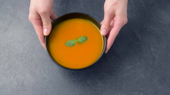 Hands Putting Bowl of Pumpkin Cream Soup on Table