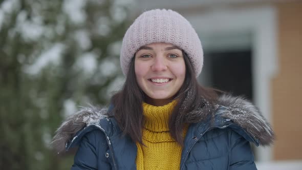 Portrait of Beautiful Young Caucasian Woman Looking at Camera Smiling with Snow Falling in Slow