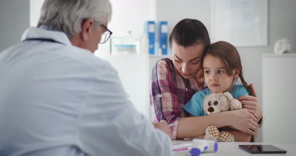 Upset Mother and Little Daughter Listening to Doctor Sitting in Clinic Office