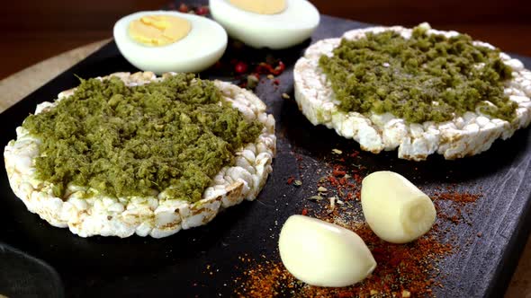 Rice Cake Toasts with Spreading Green Pesto Sauce and Boiled Eggs Rotate Slowly on Cutting Board