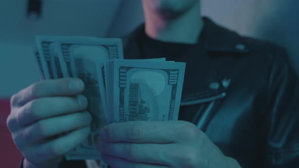 Close-up of Male Drug Dealer Counting Money Against the Background of Neon Lights of a Nightclub.