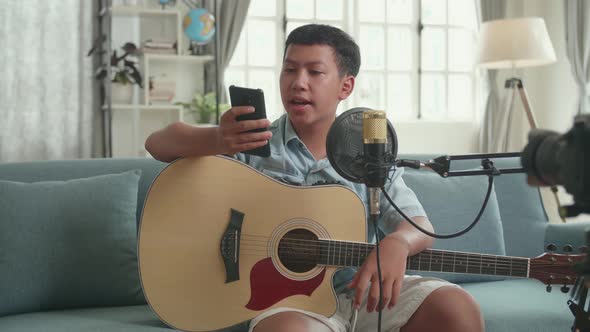 Asian Boy Is A Vlogger With Guitar Read Comment On Mobile Phone. The Boy Is Streaming