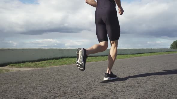 Runner Runs on a Road Near the Lake Athlete Trains in on a Sunny Day Low Angle View Triathlon