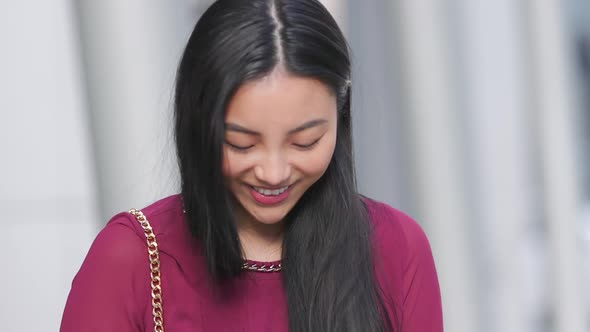 Asian woman looking down at her phone and laughing and smiling in slow motion