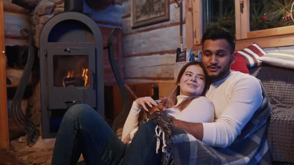 Happy Young Multiracial Couple Relaxing Near the Fireplace Covered with Blanket