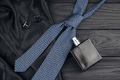 A bottle of mens cologne and cufflinks with blue tie lie on a black luxury fabric - PhotoDune Item for Sale