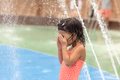 Little toddler girl standing under fountains at the playground - PhotoDune Item for Sale