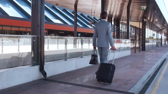 Elegant businessman walking with suitcase along the airport. Young mail entrepreneur.