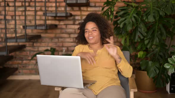 Charming AfricanAmerican Woman Sitting on the Armchair Waving at the Laptop