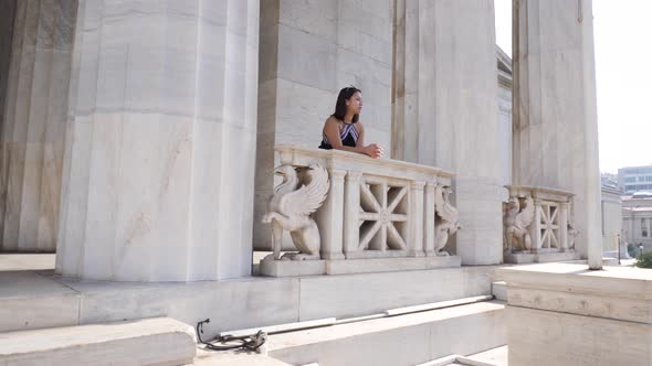 Shot of a young asian woman who leans on a balcony of an old marble building in Athen.