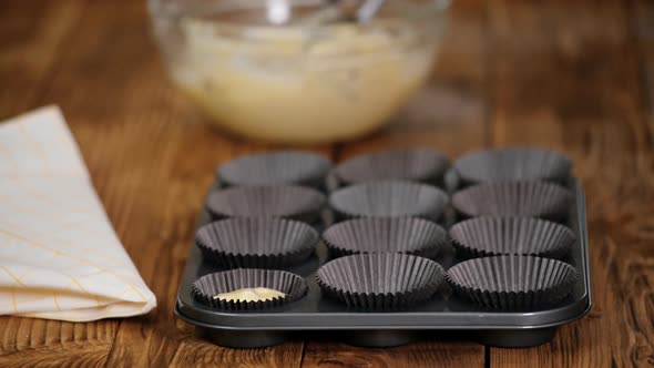 Hands pouring dough into molds for muffins on a wooden table