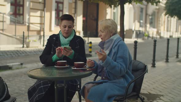 Elderly Female Couple Taking Selfie Sitting at Cafe Table Outdoors